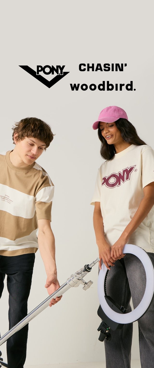 Deux jeunes personnes tenant du matériel de photographie ; l'une porte une chemise beige et blanche, l'autre un t-shirt PONY blanc et une casquette rose.