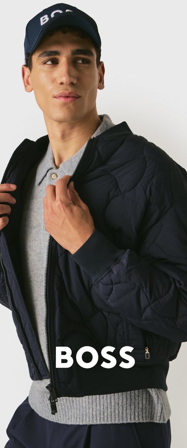 Marineblaue, gesteppte Bomberjacke mit Reißverschluss, gerippten Bündchen und einem grauen Pullover darunter, getragen mit einer marineblauen Kappe mit weißer Schrift.