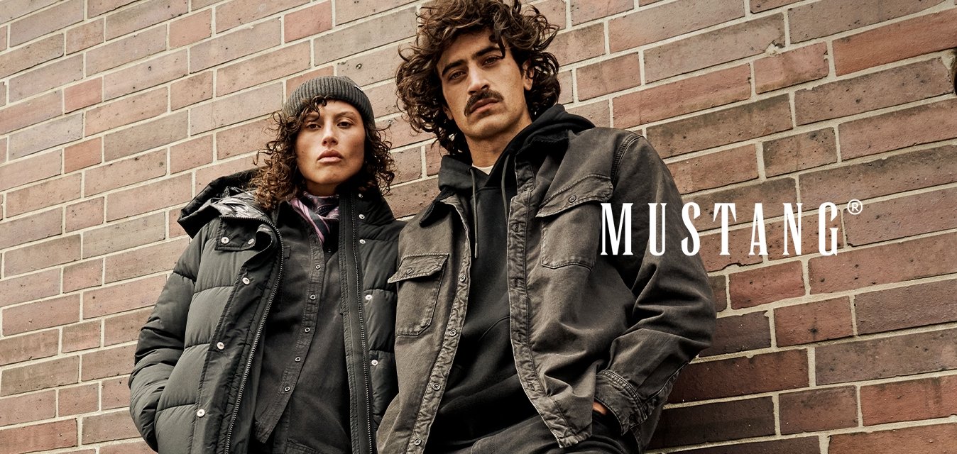 Dvě osoby v tmavém neformálním zimním oblečení a botách opírající se o cihlovou zeď, jedna má čepici a péřovou bundu.