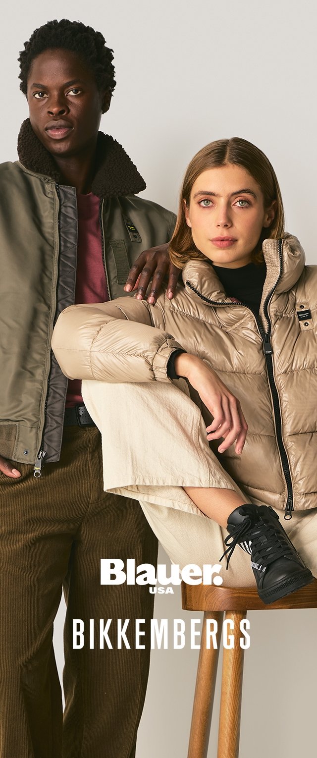 Due modelli posano fianco a fianco. Uno indossa una giacca bomber oliva; l'altro, una giacca trapuntata beige chiaro. Entrambe presentano materiali e textures distinti.