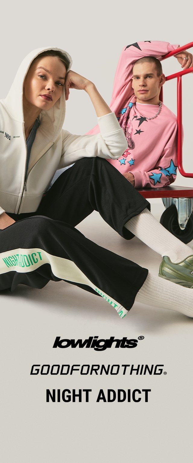 Una mujer con una sudadera blanca con capucha y pantalones negros, y un hombre con una sudadera rosa con estrellas sentados en un carrito rojo contra un fondo liso.