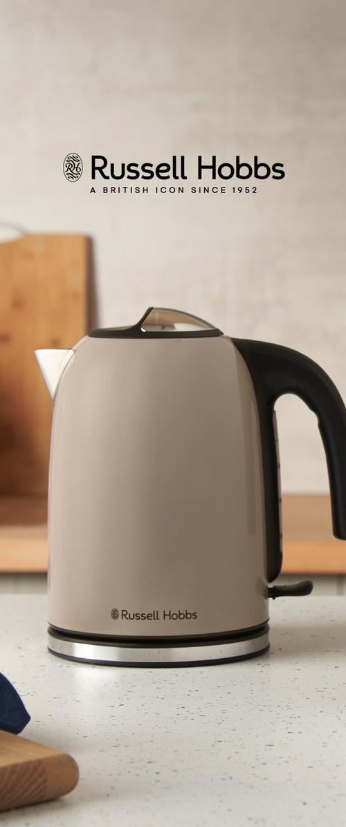 Hervidor eléctrico beige y negro Russell Hobbs sobre una encimera de cocina con tablas de cortar al fondo, logotipo y eslogan de la marca arriba.