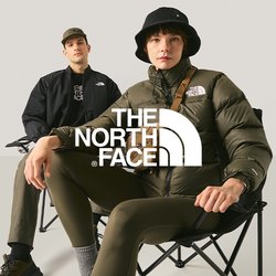 Dva mladí dospělí sedící na skládacích židlích na jednobarevném světle pozadí, jeden má na sobě černý klobouk typu bucket a prošívanou bundu.