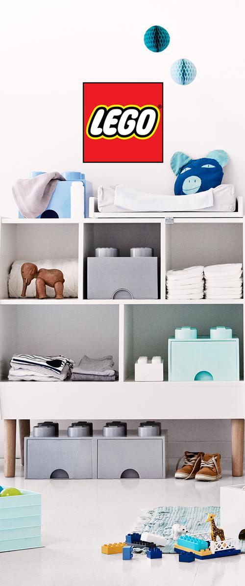 Cuarto de juegos infantil con cajas de almacenamiento de LEGO, cojín de peluche, ropa doblada, juguete de elefante de madera, zapatos y piezas de LEGO esparcidas en el suelo.