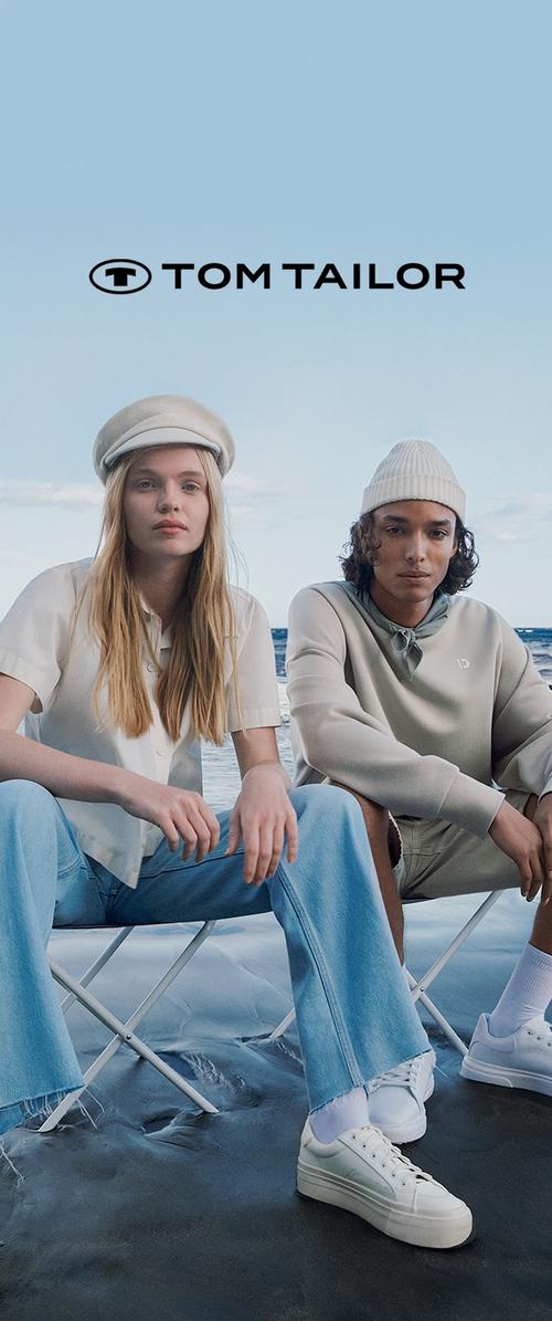 Deux personnes sont assises sur des chaises pliantes au bord de l'océan. L'une porte une chemise blanche à manches courtes et un jean flare en denim clair. L'autre porte un sweat à capuche gris et un bonnet blanc.
