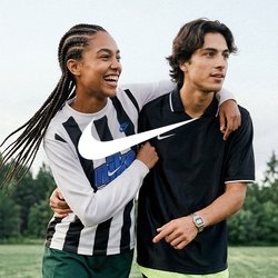 Dva mladí lidé chodí po fotbalovém hřišti, jeden má paži přes ramena druhého, oba se usmívají a jsou oblečeni ve sportovním oblečení.