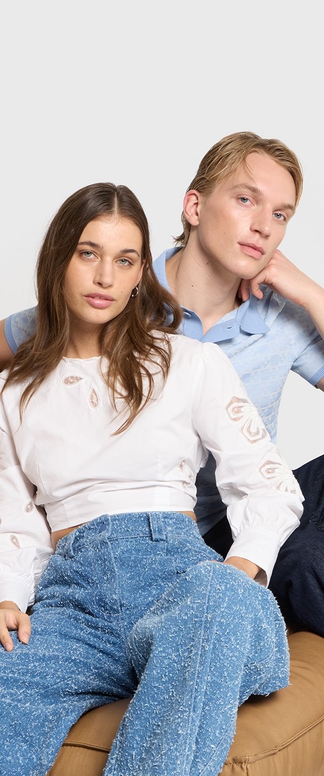 Biała bluzka z długim rękawem z haftowanymi akcentami, niebieskie szerokie spodnie o fakturze oraz dopasowana niebieska koszula z kołnierzykiem. Casualowe, współczesne style.