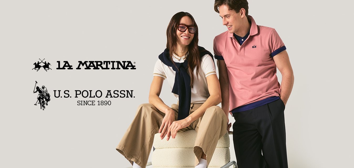 Mladá žena sedící na židli, nosící brýle a neformální oblečení, mladý muž stojící vedle ní, usmívající se a opírající se o židli.