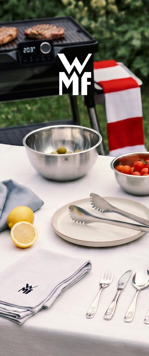 Table extérieure avec bols en acier inoxydable, couverts, pinces, citrons et viande grillée cuisinée sur un gril électrique à proximité.