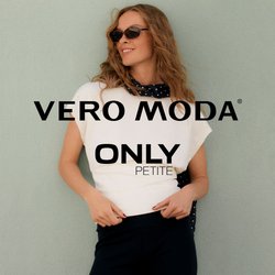 Žena s vlnitými vlasy, která má na sobě sluneční brýle, bílý top, černé tříčtvrteční kalhoty a černý šátek s bílými puntíky, pózuje u světle zelené zdi.