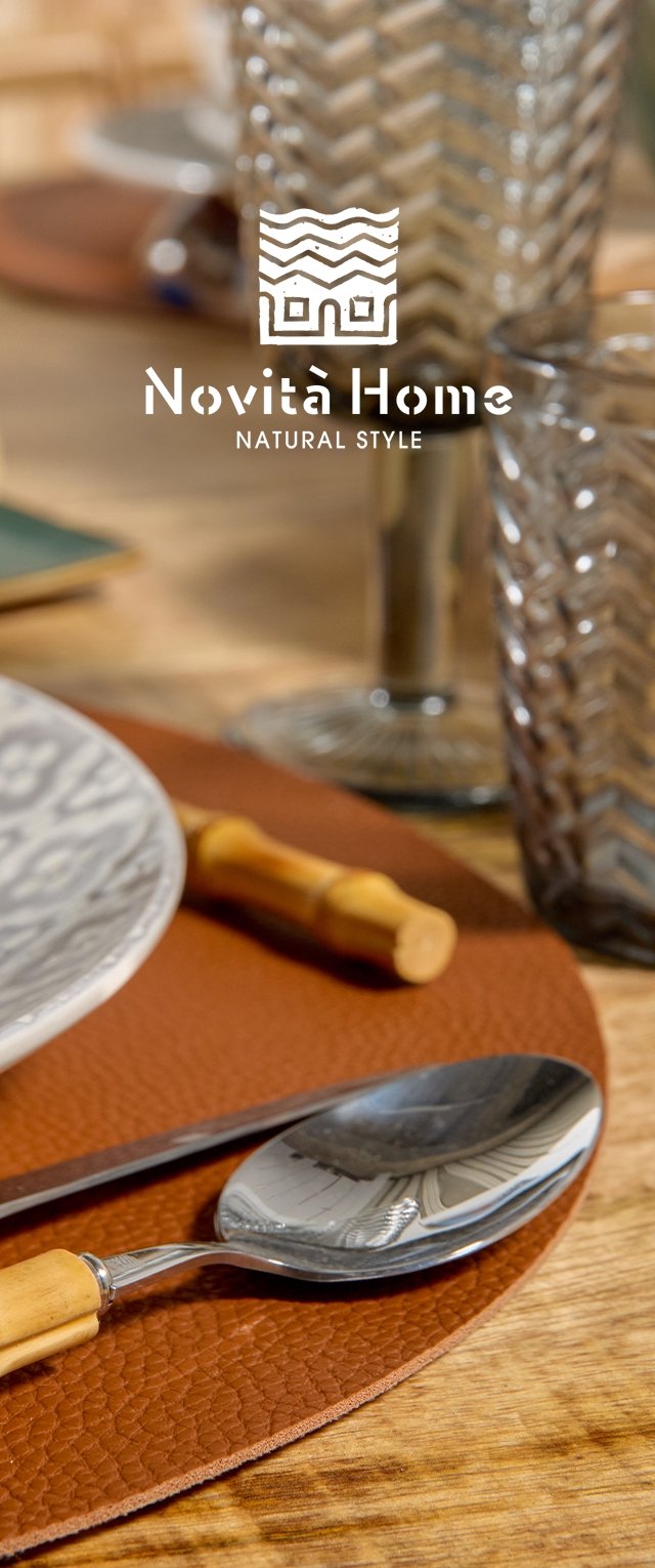 Cuchara y cuchillo con mangos de madera sobre un individual marrón texturizado, junto a un plato blanco estampado y cristalería de fondo.