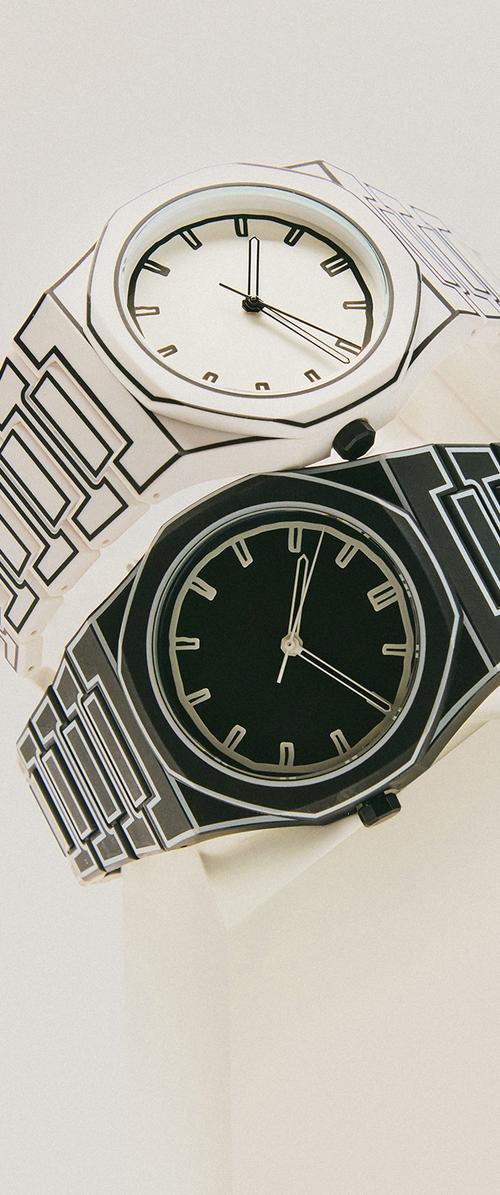 Dos relojes de pulsera geométricos dispuestos en ángulo diagonal; uno blanco con detalles negros, y uno negro con detalles blancos, ambos mostrando aproximadamente las 12:15.