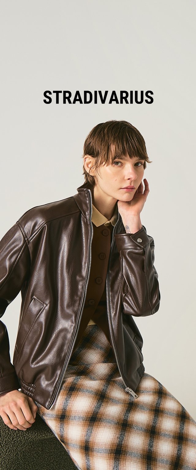 Young woman wearing a brown leather jacket, plaid skirt, and beige top, posing with hand near face under "STRADIVARIUS" text on a plain background.