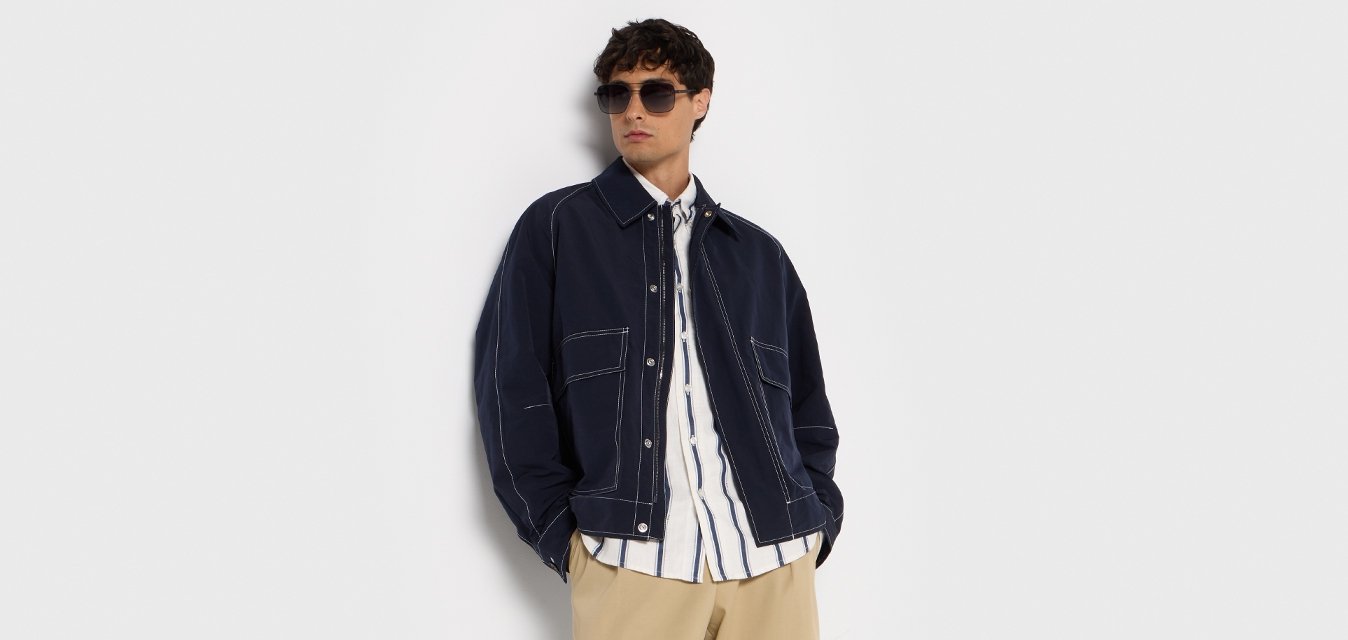 Námořnická bomberka přes bílé a námořnické pruhované tričko, doplněná béžovými kalhotami a krémovými teniskami se světlou hnědou podrážkou.