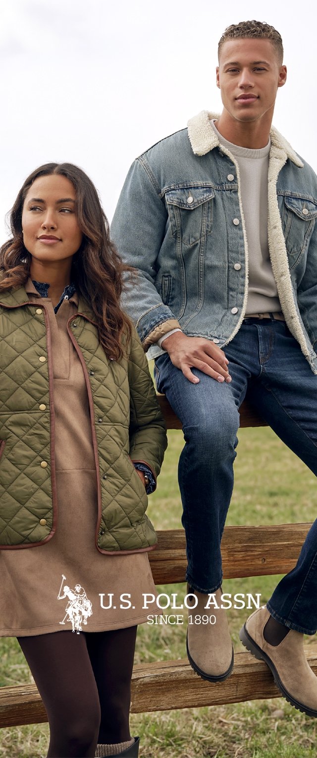 Femme portant une veste matelassée verte et une robe se tient à côté d'un homme en veste en denim sherpa bleue et jeans assis sur une clôture en bois à l'extérieur.