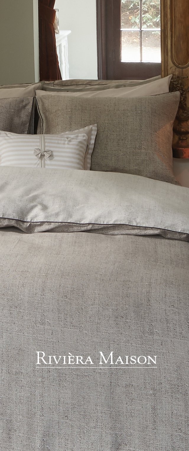 Conjunto de ropa de cama gris texturizado que incluye múltiples cojines, entre ellos un cojín con rayas y detalle de lazo. Diseño minimalista.