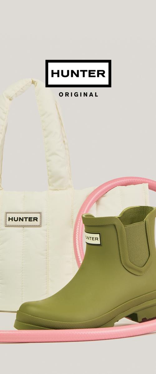 Botte de pluie Hunter mi-cheville en vert olive à côté d'un sac fourre-tout matelassé crème de la marque Hunter, avec un tube circulaire rose en arrière-plan.
