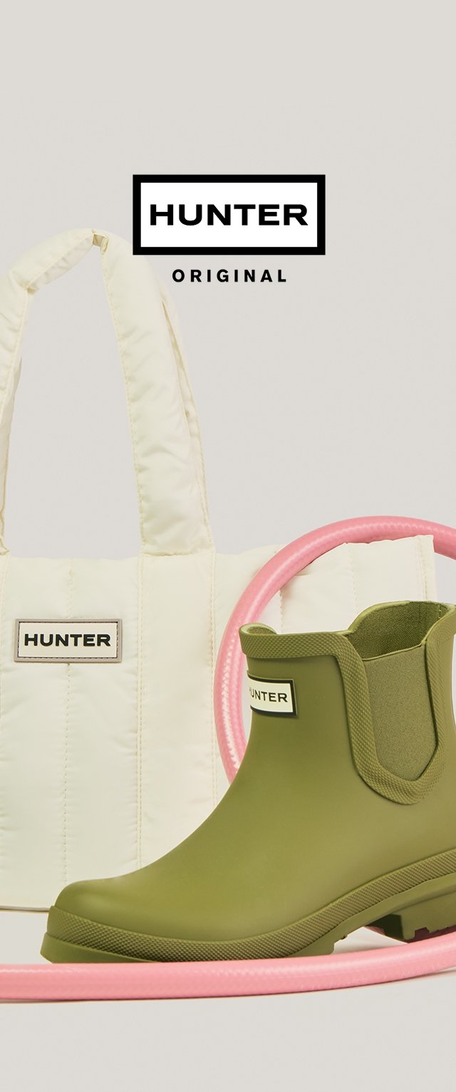 Olive zielony kalosz Hunter za kostkę obok kremowej pikowanej torby Hunter typu tote, z różową okrągłą tubą w tle.