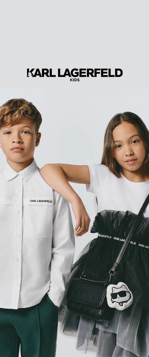 Niño con camisa blanca y pantalones verdes está junto a una niña con vestido blanco y negro con bolso y la marca Karl Lagerfeld encima de ellos.