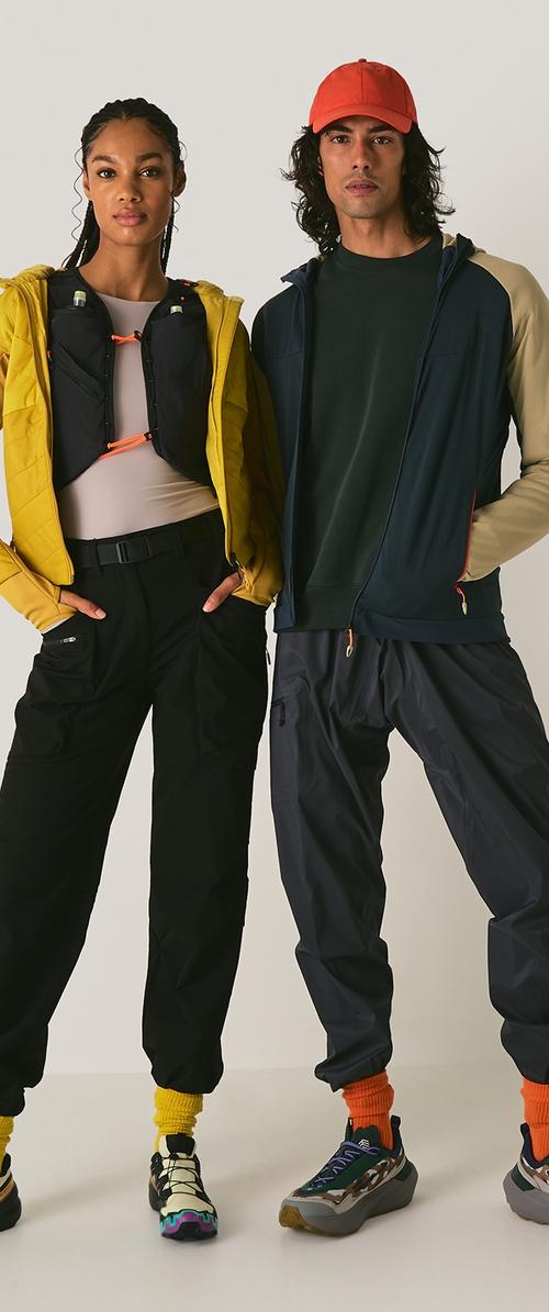 Deux mannequins portent des vêtements de sport : une veste en duvet jaune, un pantalon noir, une chemise vert foncé et des baskets colorées avec des textures et des accents visibles.