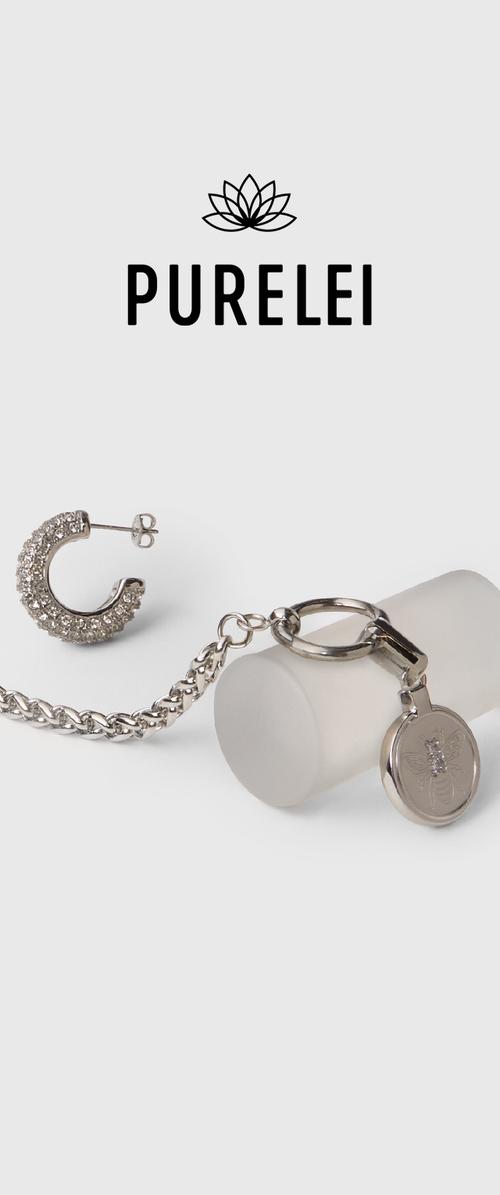 Pendiente de aro en tono plateado con piedras de rhinestone transparentes, junto a un llavero de metal pulido adjunto a un objeto cilíndrico mate.