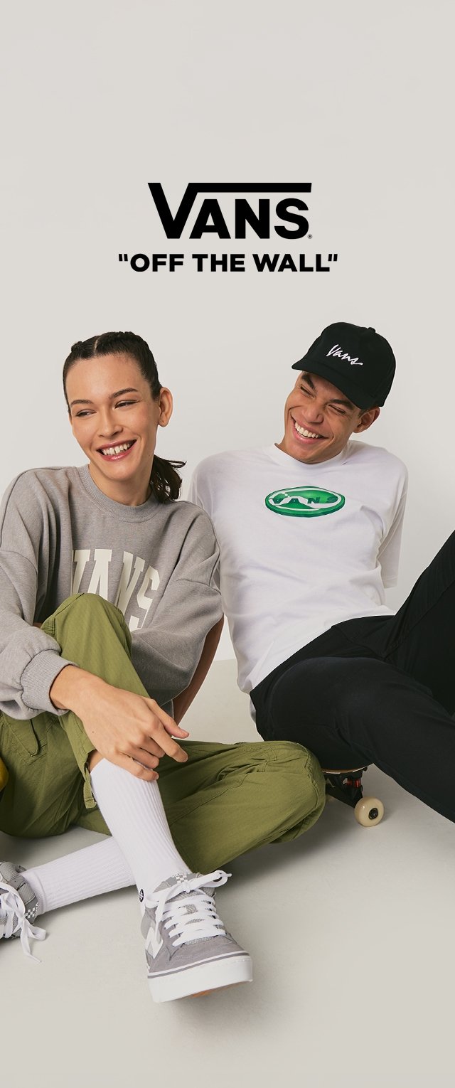 Grauer Pullover mit "VANS"-Schriftzug, grünes T-Shirt mit Logo, grüne Hose, graue Sneakers; lässiger Stil, entspannte Passform und weiße Socken.