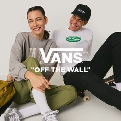 Dva mladí lidé sedí na podlaze v neformálním oblečení, jeden má skateboard a žlutý batoh, usmívají se a nahlížejí si blízko u sebe.