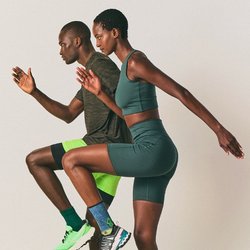 Dva sportovci ve sportovním oblečení provádějí cvičení s vysokým kolenem na jednobarevném pozadí, což zdůrazňuje fitness a koordinaci.