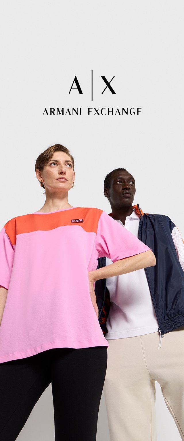 T-shirt oversize rosa con accenti arancioni e logo, abbinato a una giacca blu navy su un top bianco e pantaloni beige chiaro.