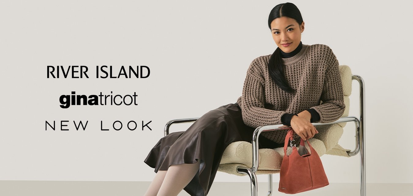 Žena v hnědém pleteném svetru a kožené sukni sedí na moderní chromové a textilní židli, drží malou červenou kabelku a usmívá se do kamery.