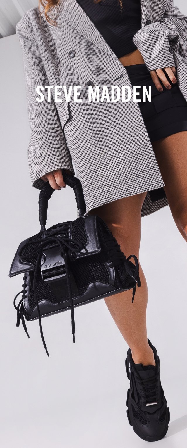 Frau trägt schwarze Shorts, Hahnentritt-Blazer und schwarze Sneakers und hält eine schwarze Steve Madden Handtasche an den Griffen.
