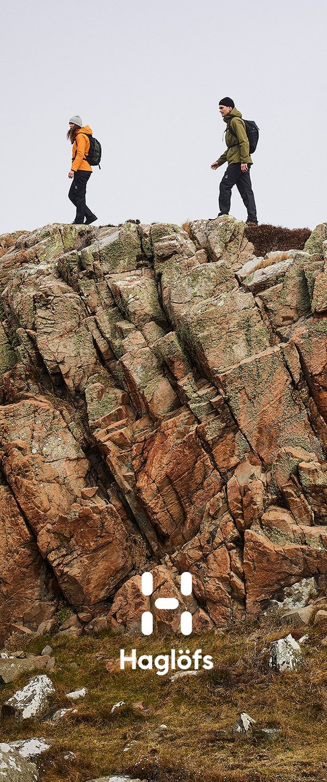 Zwei Wanderer auf felsigem Terrain, gekleidet in einen orangefarbenen Hoodie und eine grüne Jacke, mit Rucksäcken. Der Hintergrund zeigt strukturierte braune und graue Steine.