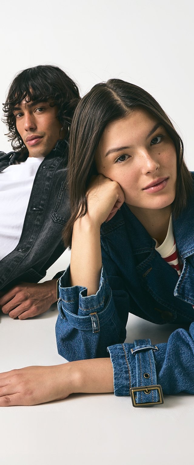 Dos modelos posan de manera casual. La mujer lleva una chaqueta de mezclilla azul sobre una blusa clara; el hombre tiene una chaqueta de mezclilla negra sobre una camiseta blanca.