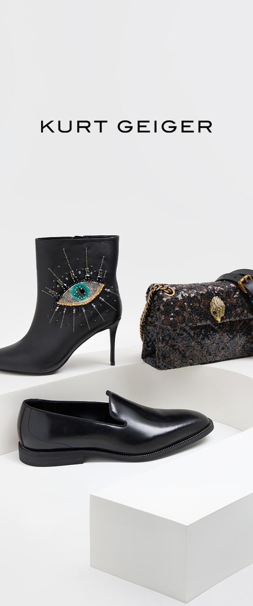 Bota negra de tobillo con diseño de ojo y detalles plateados, bolso negro de lentejuelas con cierre dorado y elegantes mocasines negros exhibidos sobre cubos blancos.