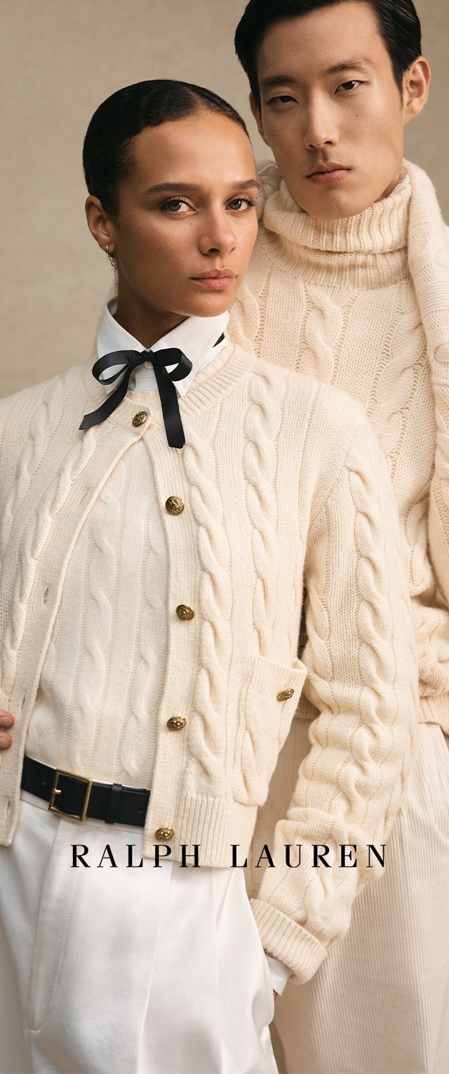 Kreemivärvilised kaeluseta kudumid kuldsete nööpidega, valge krae ja musta lipsuga särk ning ribakoes kreemivärviline kõrge kaelusega sviiter taustal.