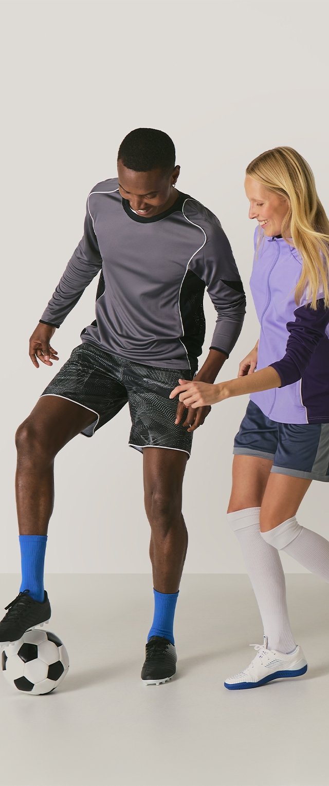 Deux personnes interagissent sur un fond clair ; l'une porte un t-shirt à manches longues gris et un short noir à motifs avec des chaussettes bleues, l'autre un haut violet et un short gris.