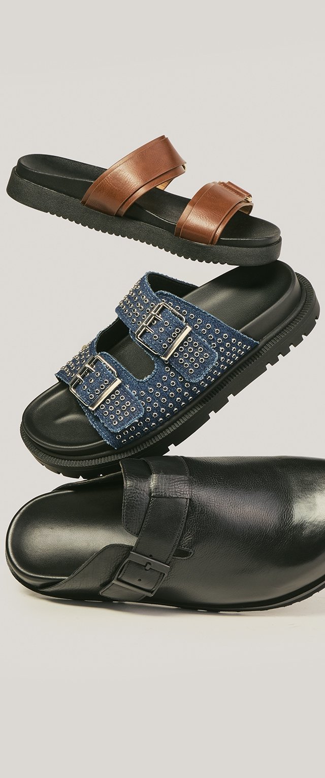 Trois sandales à enfiler : cuir marron avec deux brides, tissu bleu clouté avec boucles, et cuir noir avec une boucle latérale, disposées verticalement.