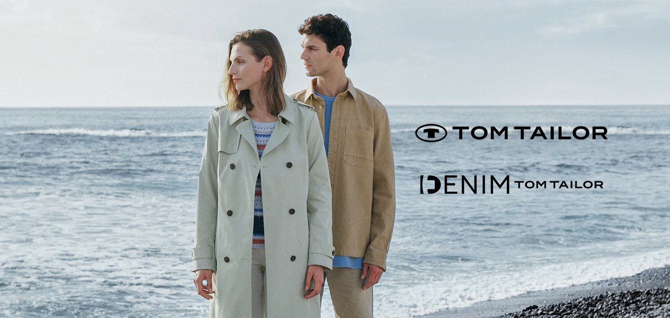 Světle zelený trench coat, béžová košile, bílé kalhoty a hnědé boty. Oba kousky jsou neformální, s měkkými texturami na pozadí kamenité pláže.