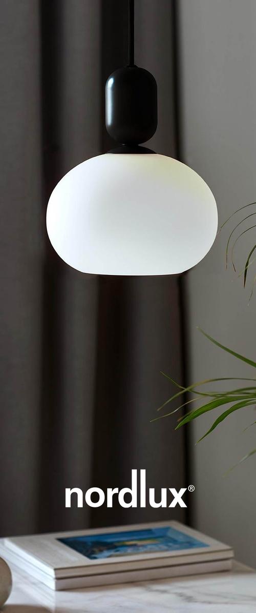 Runde, frostierte Glaspendelleuchte in Weiß mit schwarzem Oberteil und Aufhängeschnur. Minimalistisches Design, im Vordergrund eines grauen Vorhangs aufgehängt.