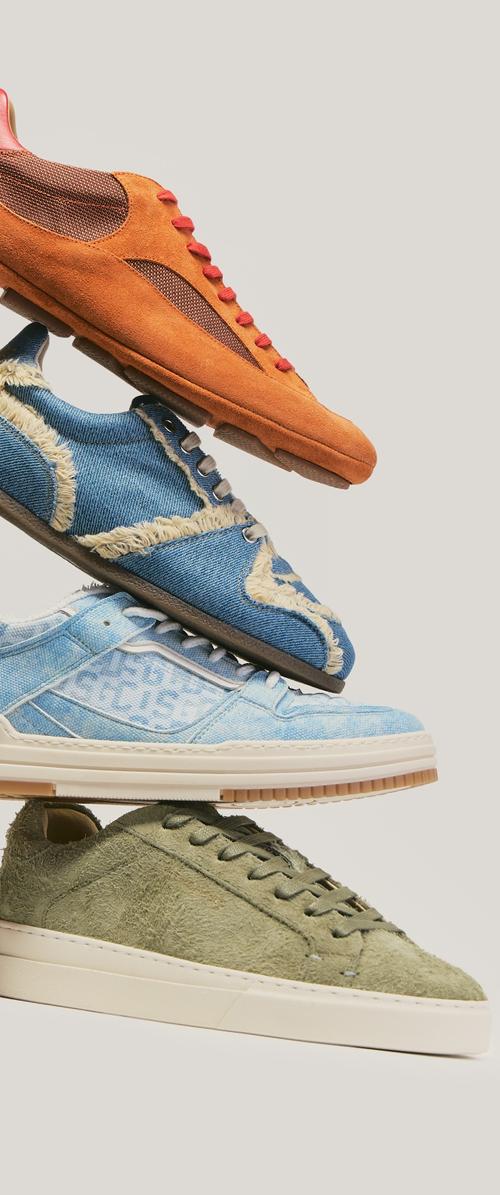 Pila de cuatro zapatillas casuales en ante naranja, vaquero azul con flecos, tejido texturizado azul claro y ante verde oliva sobre un fondo neutro.
