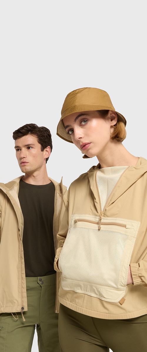 Jachete ușoare beige cu buzunare din plasă, închidere cu fermoar și pălărie tip bucket bej asortată; cămașă și pantaloni verzi închis pe model.