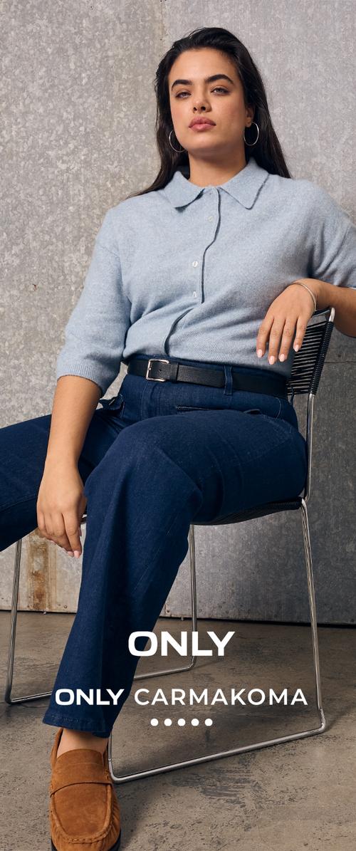 Femme aux longs cheveux foncés porte un pull bleu clair, un pantalon bleu foncé et des mocassins bruns, assise avec assurance sur une chaise devant un mur gris.