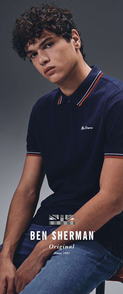 Navyblaue Poloshirt mit einem gerippten Kragen, der rot-weiße Streifen aufweist. Logo auf der Brust; strukturiertes Material; Modell sitzt vor einem grauen Hintergrund.