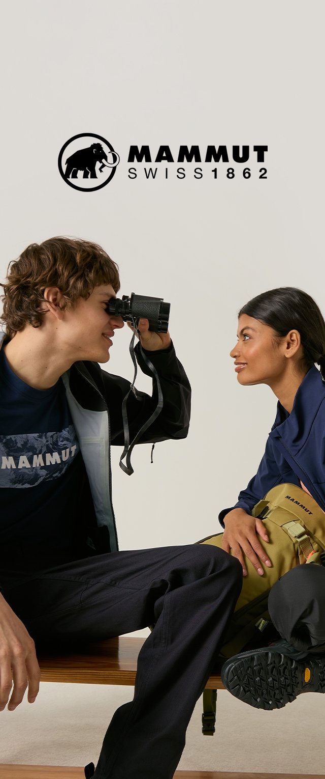 Joven mira a mujer que sonríe a través de unos binoculares, ambos vestidos con ropa de exterior, sentados en un banco con el logo de Mammut encima de ellos.