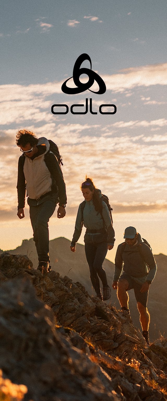 Drei Wanderer steigen während des Sonnenuntergangs ein felsiges Terrain hinauf. Sie tragen unterschiedliche Outdoor-Bekleidung, wobei das Logo "odlo" über ihnen sichtbar ist.
