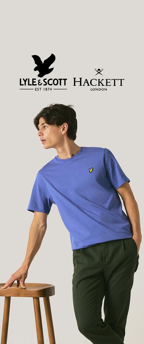 Joven con una camiseta azul de Lyle & Scott y pantalones oscuros apoyado en un taburete de madera, con los logotipos de Lyle & Scott y Hackett arriba.
