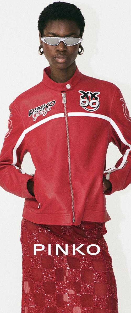 Veste zippée rouge avec des accents et un logo blancs. Portée par-dessus une jupe rouge transparente à sequins. Les accessoires comprennent des lunettes de soleil argentées et des boucles d'oreilles circulaires.