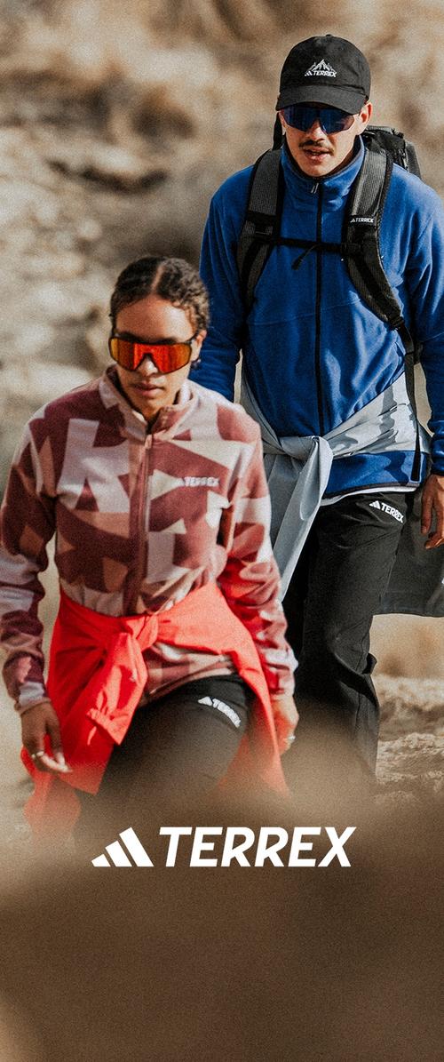 Deux randonneurs portant des vêtements d'extérieur et des lunettes de soleil marchent sur un sentier rocheux, l'un d'eux portant un sac à dos avec la marque "TERREX" visible.
