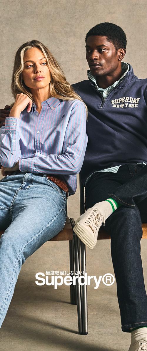 Zwei sitzende Modelle tragen legere Kleidung: ein blau-rosa gestreiftes Hemd und einen dunkelblauen Sweatshirt. Die Denim-Jeans haben eine lockere Passform.