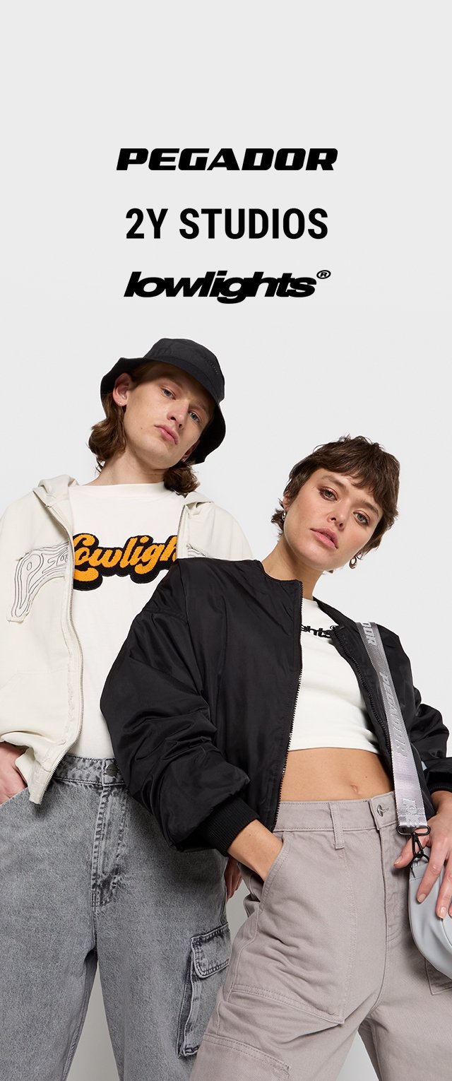 Dos modelos posan con ropa urbana casual: uno lleva una sudadera blanca, jeans grises y un sombrero de cubo negro; el otro viste una chaqueta negra, un top corto y pantalones claros.